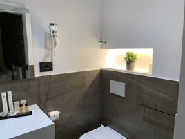 Egy modern fürdőszoba zuhanyzóval, törölközőtartóval, virágtartóban lévő növényekkel és a mosdóban elhelyezett piperecikkekkel.