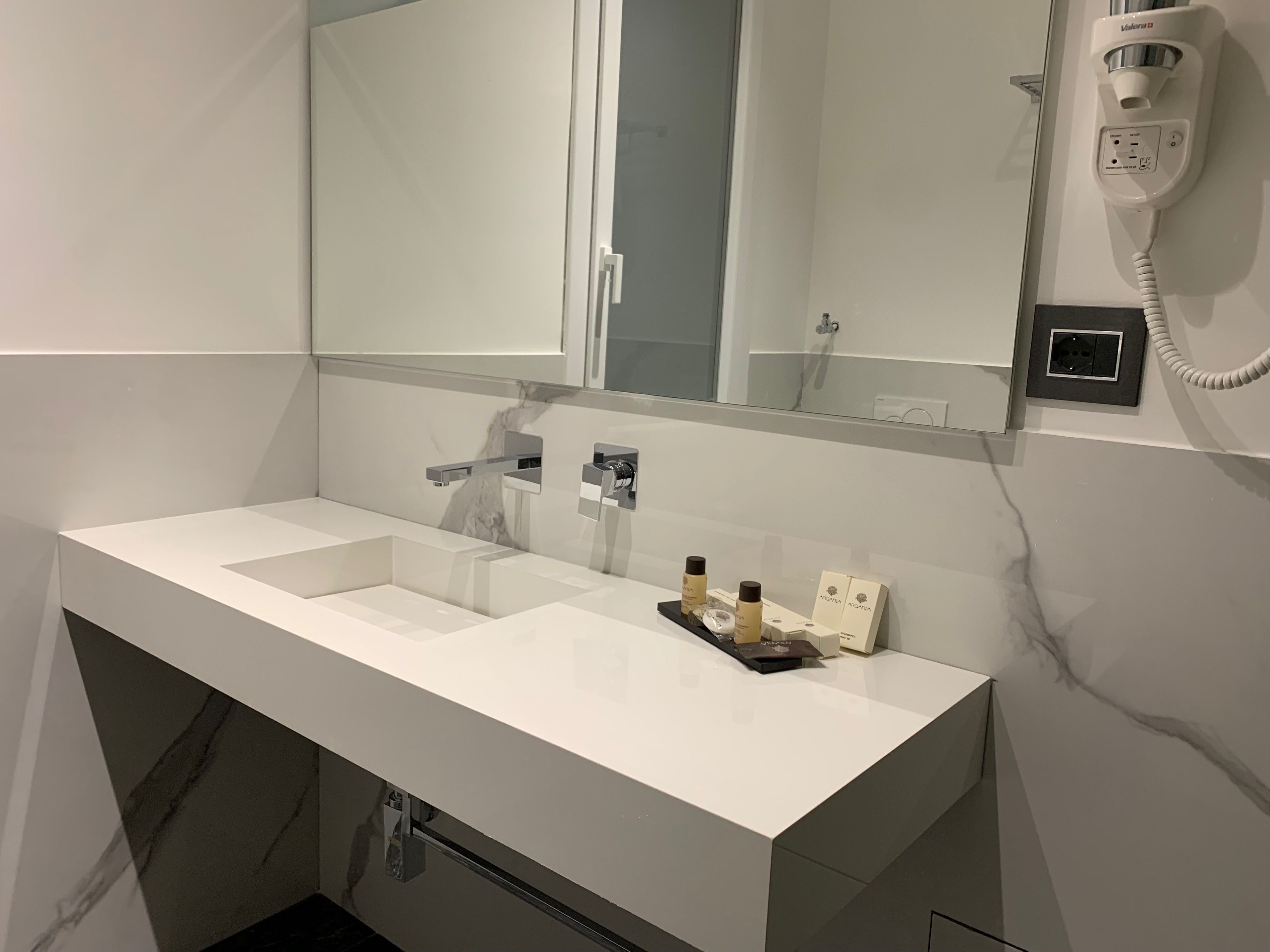 Ein modernes Badezimmer mit einem großen weißen Waschbecken, einem Spiegel und einem an der Wand montierten Fön.