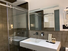 Un baño moderno con ducha de vidrio, lavamanos blanco y un espejo grande.