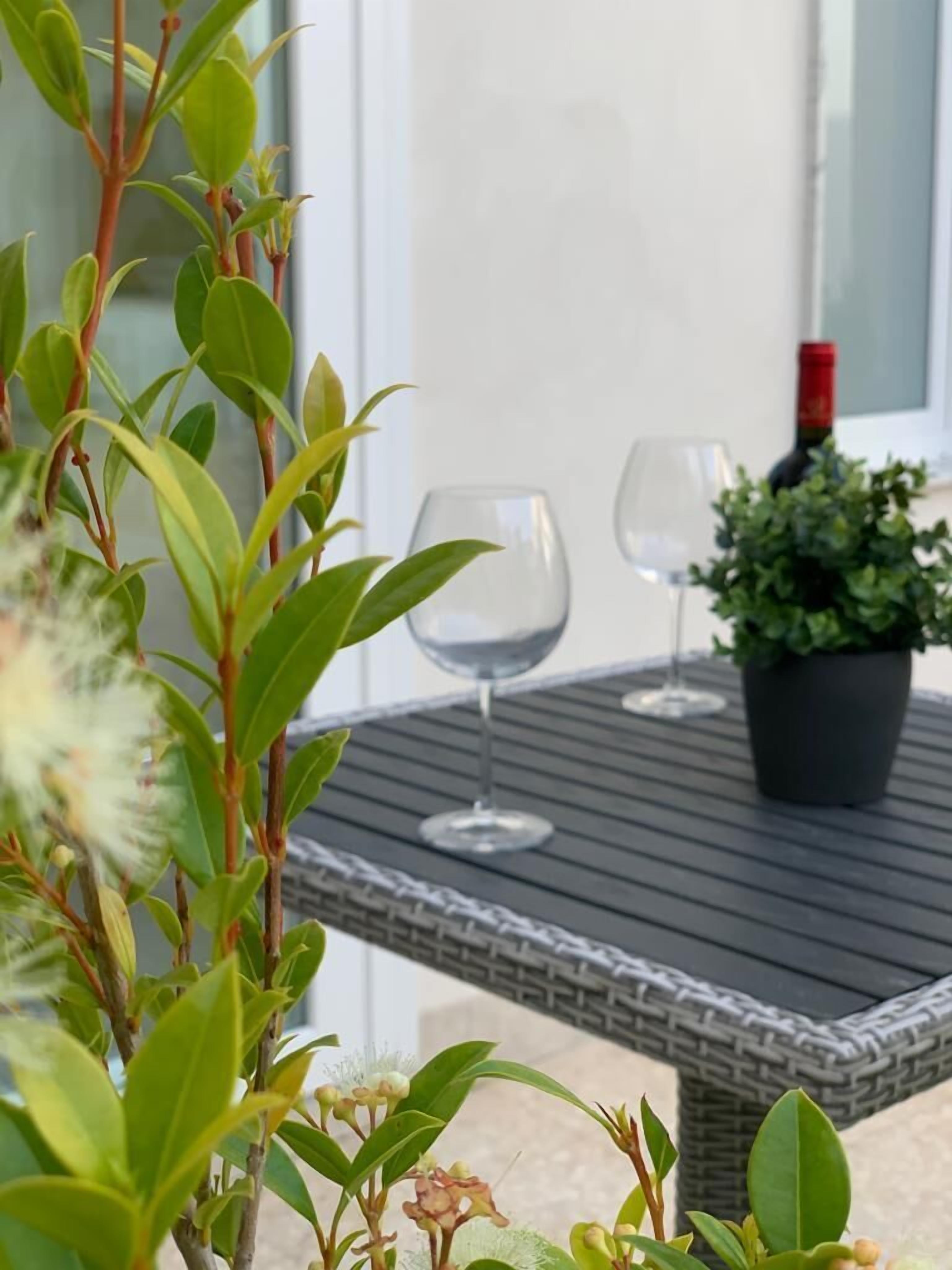 A patio with a table, two wine glasses, and a potted plant.