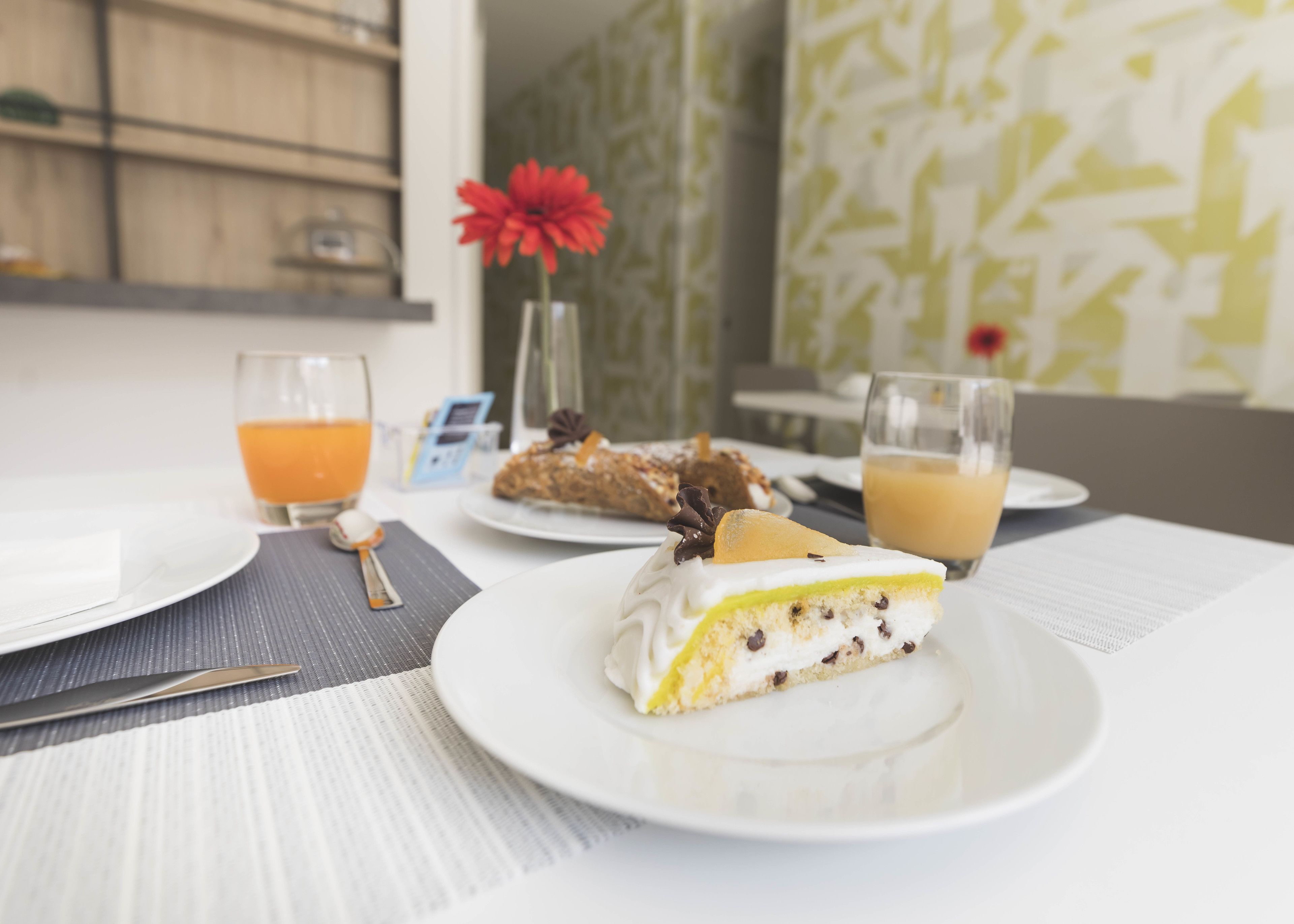 Et morgenbord med et stykke kage, et glas appelsinjuice og et glas kaffe på et bord.