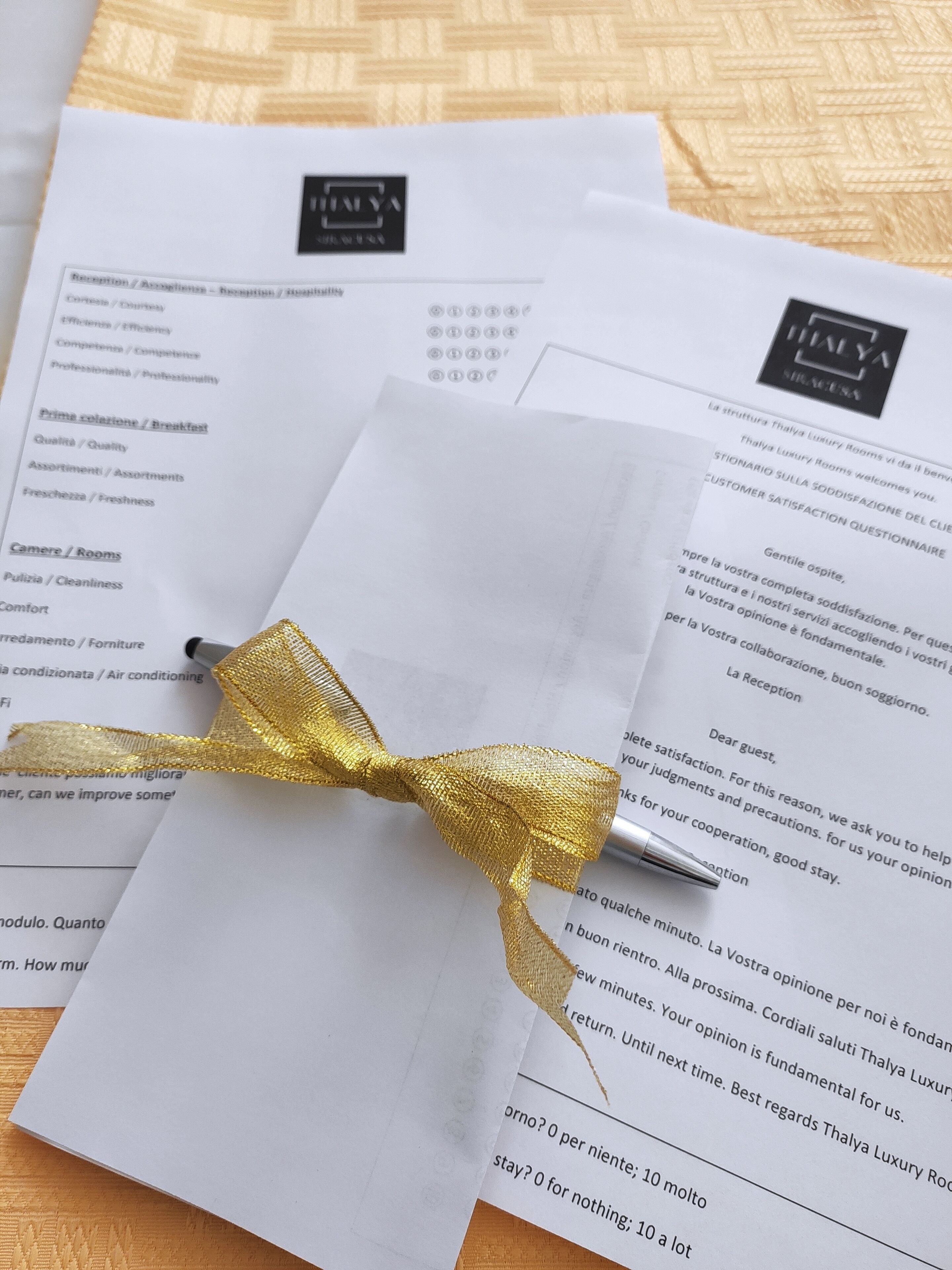 Een hotelkamer brochure met een gouden lint erom, geplaatst op een gestructureerde stoffen achtergrond.