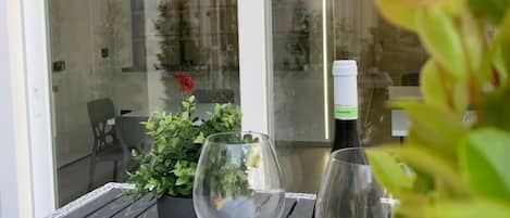 A table with two wine glasses and a bottle of wine, a potted plant, and a glass door leading to an outdoor area.