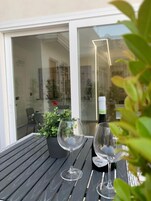 Een tafel met twee wijnglazen en een wijnfles, een potplant en een glazen deur die leidt naar een buitenruimte.