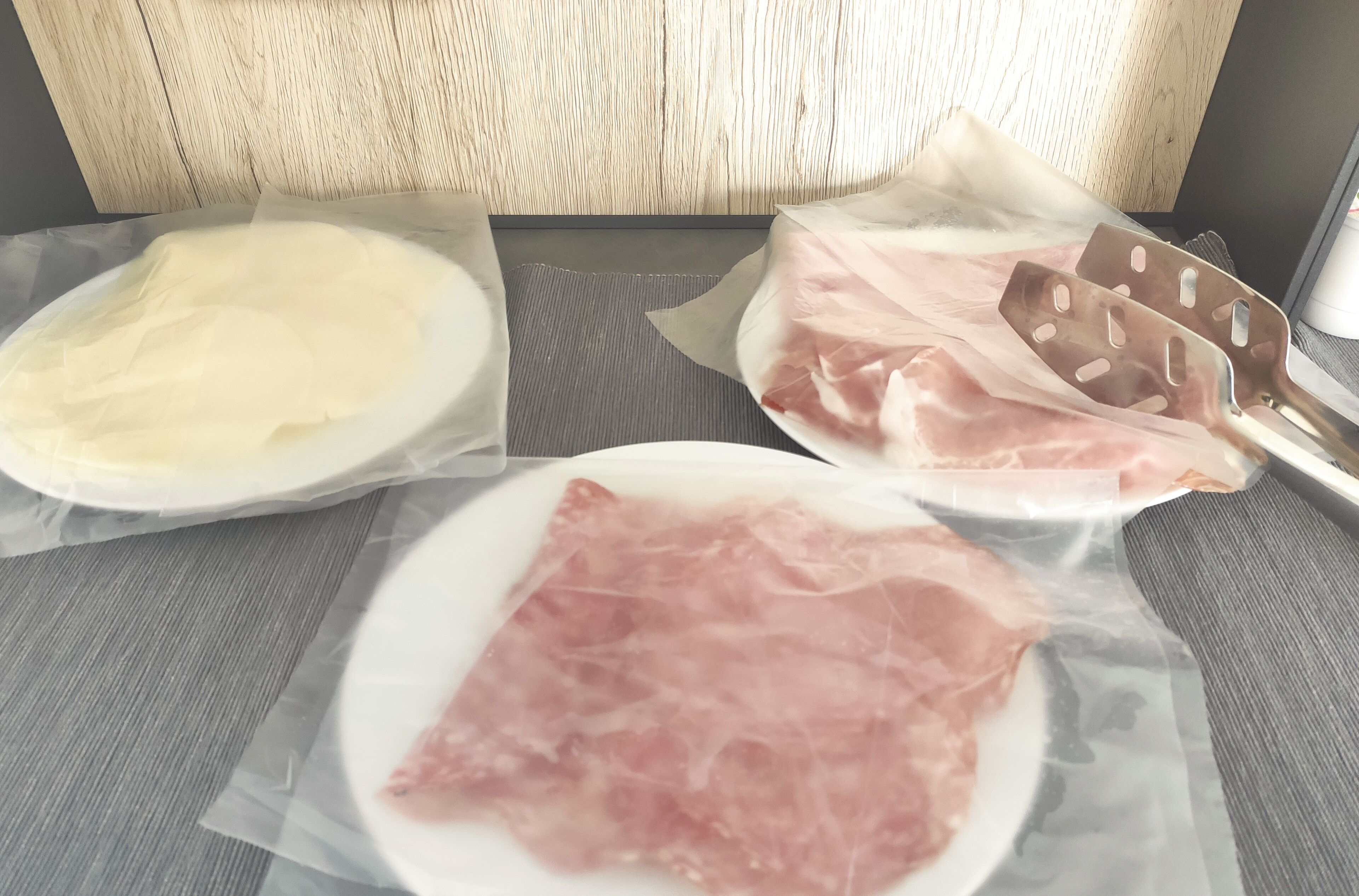 A table with three plates of food, each covered with plastic wrap.