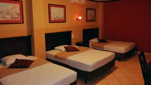 A hotel room with three single beds, a wall-mounted air conditioner, and framed pictures on the walls. - Hotel Merliot (Antiguo Cuscatlán)