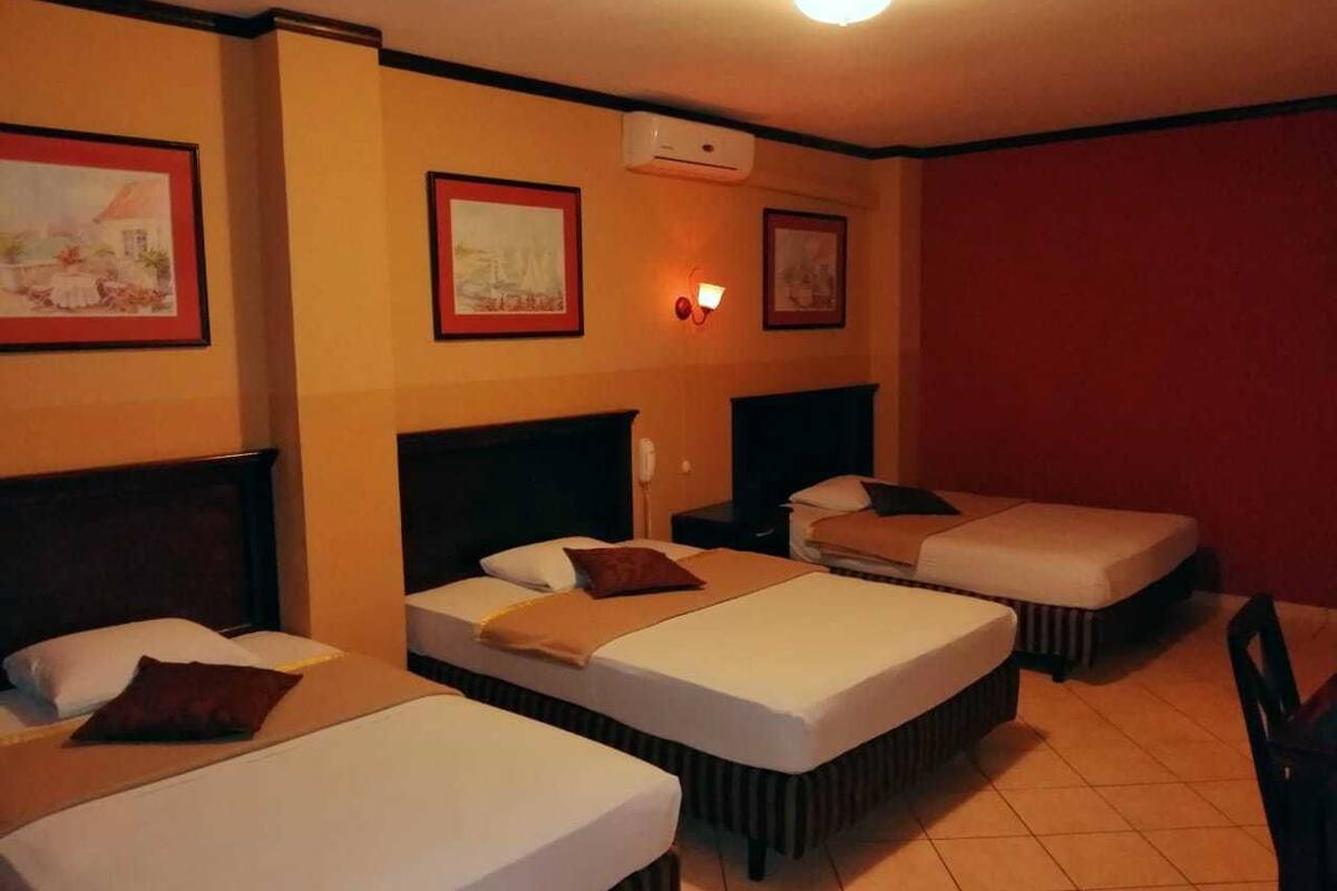 Ein Hotelzimmer mit drei Einzelbetten, einer Wandklimaanlage und gerahmten Bildern an den Wänden.