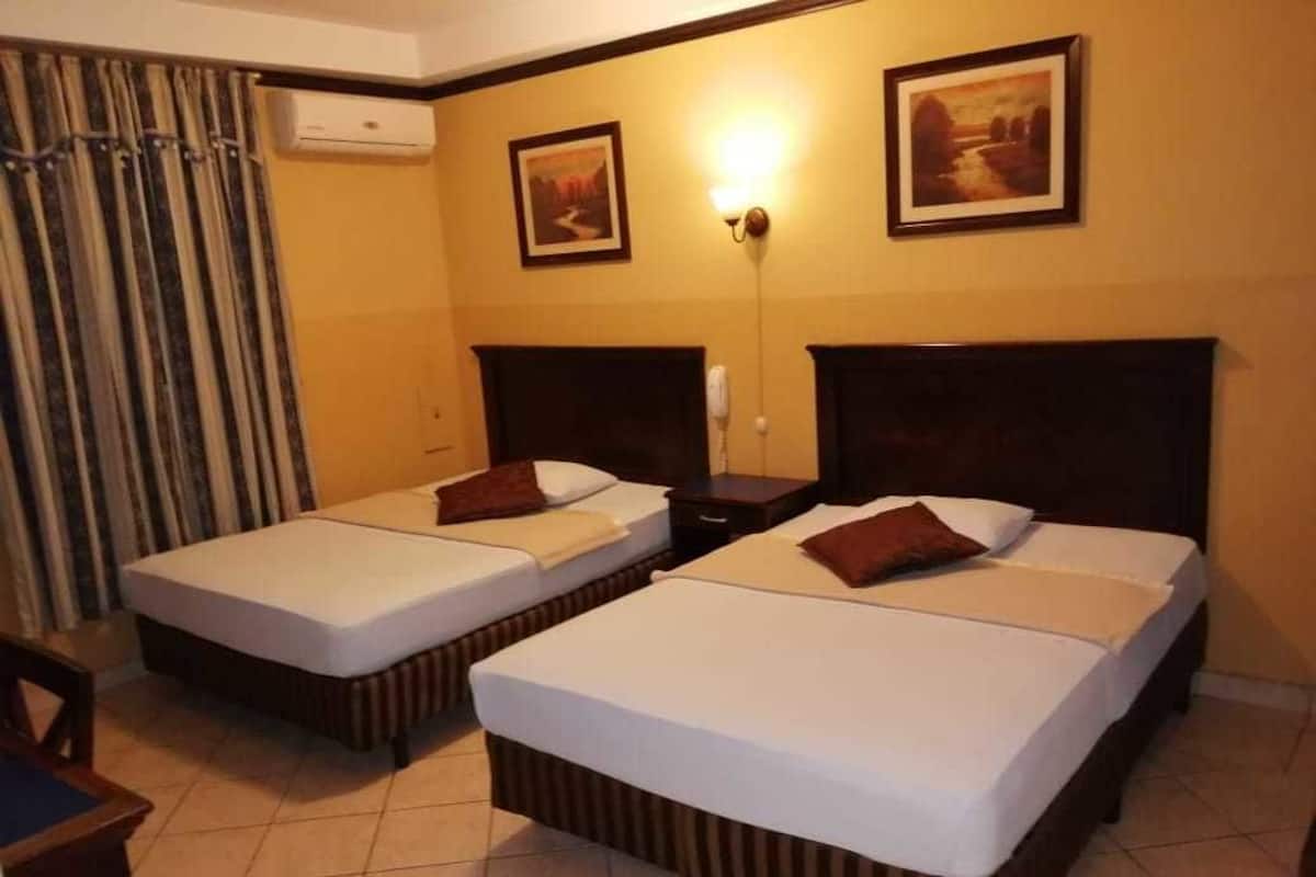 Ein Hotelzimmer mit zwei Einzelbetten, einem Schreibtisch, einem Stuhl und einem Fenster mit Vorhängen.