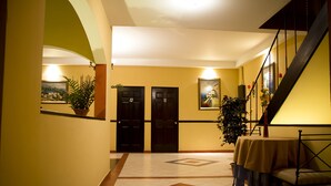 A hallway with two black doors, a staircase, and a table with a chair. - Hotel Merliot (Antiguo Cuscatlán)