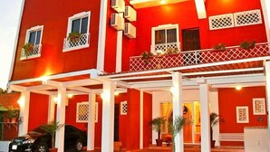 A red hotel with multiple balconies and air conditioning units. - Hotel Merliot (Antiguo Cuscatlán)
