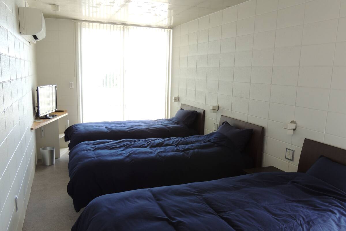 A hotel room with two beds, a TV on a shelf, and a window with blinds.