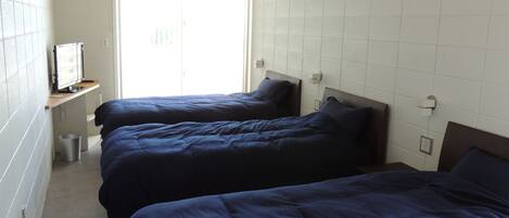 Una habitación de hotel con dos camas, un televisor en un estante y una ventana con persianas.