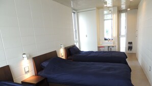 A hotel room with three beds, a small desk, and a window.
