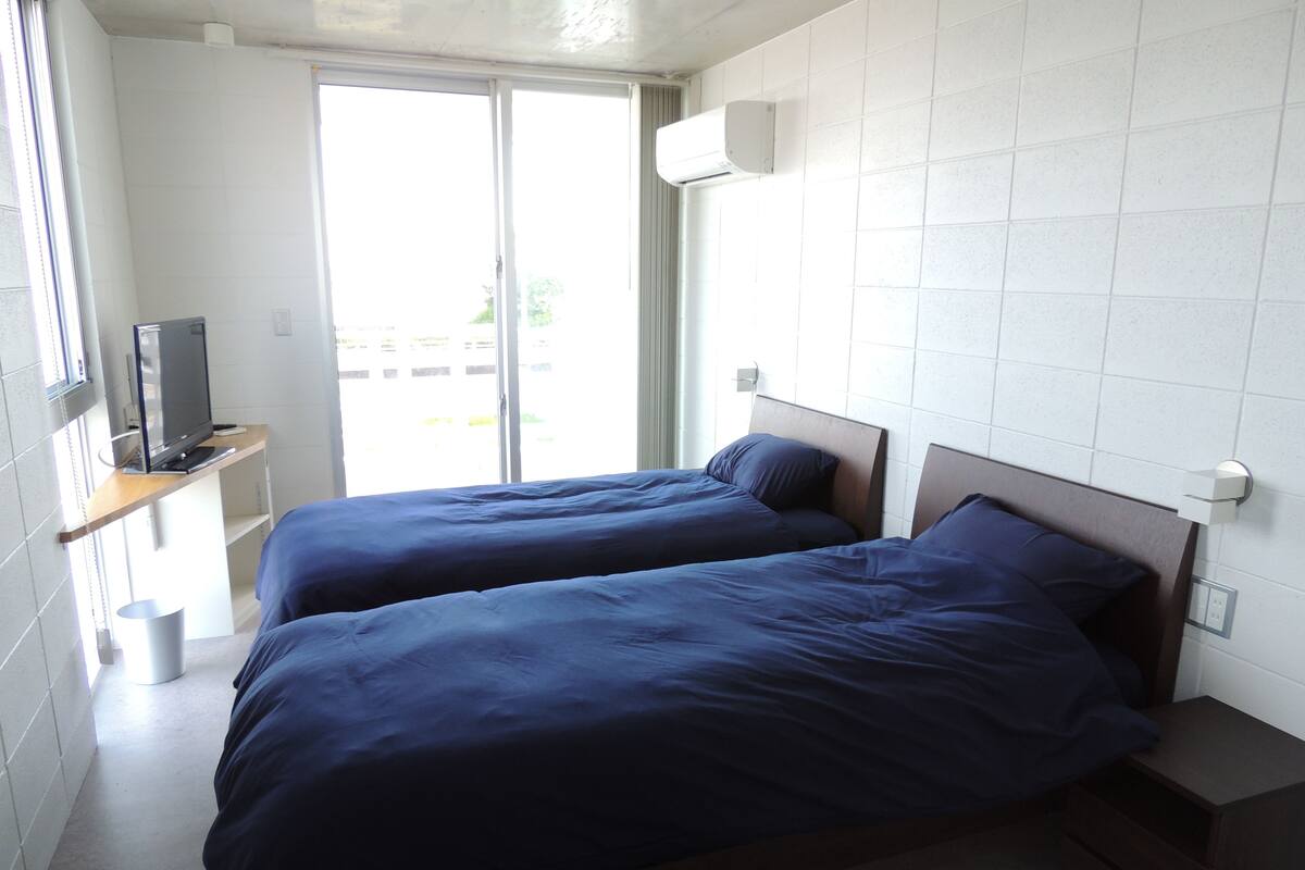 A hotel room with two beds, a TV on a shelf, and a window with a view of buildings.