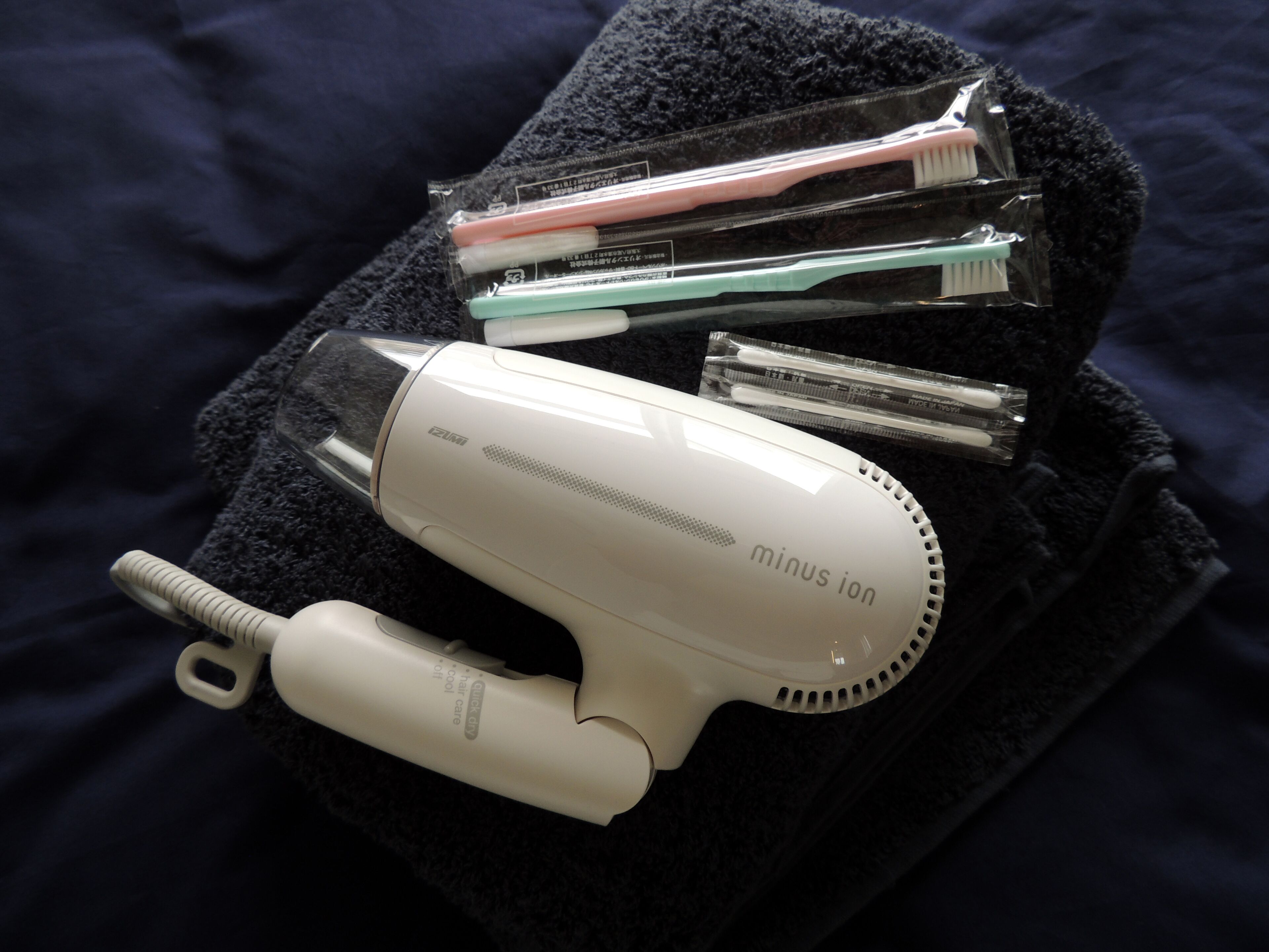 A hair dryer, toothbrushes, and a razor on a dark towel.