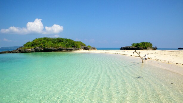 A beach with clear turquoise water, white sandy shore, and lush green vegetation on small islands.