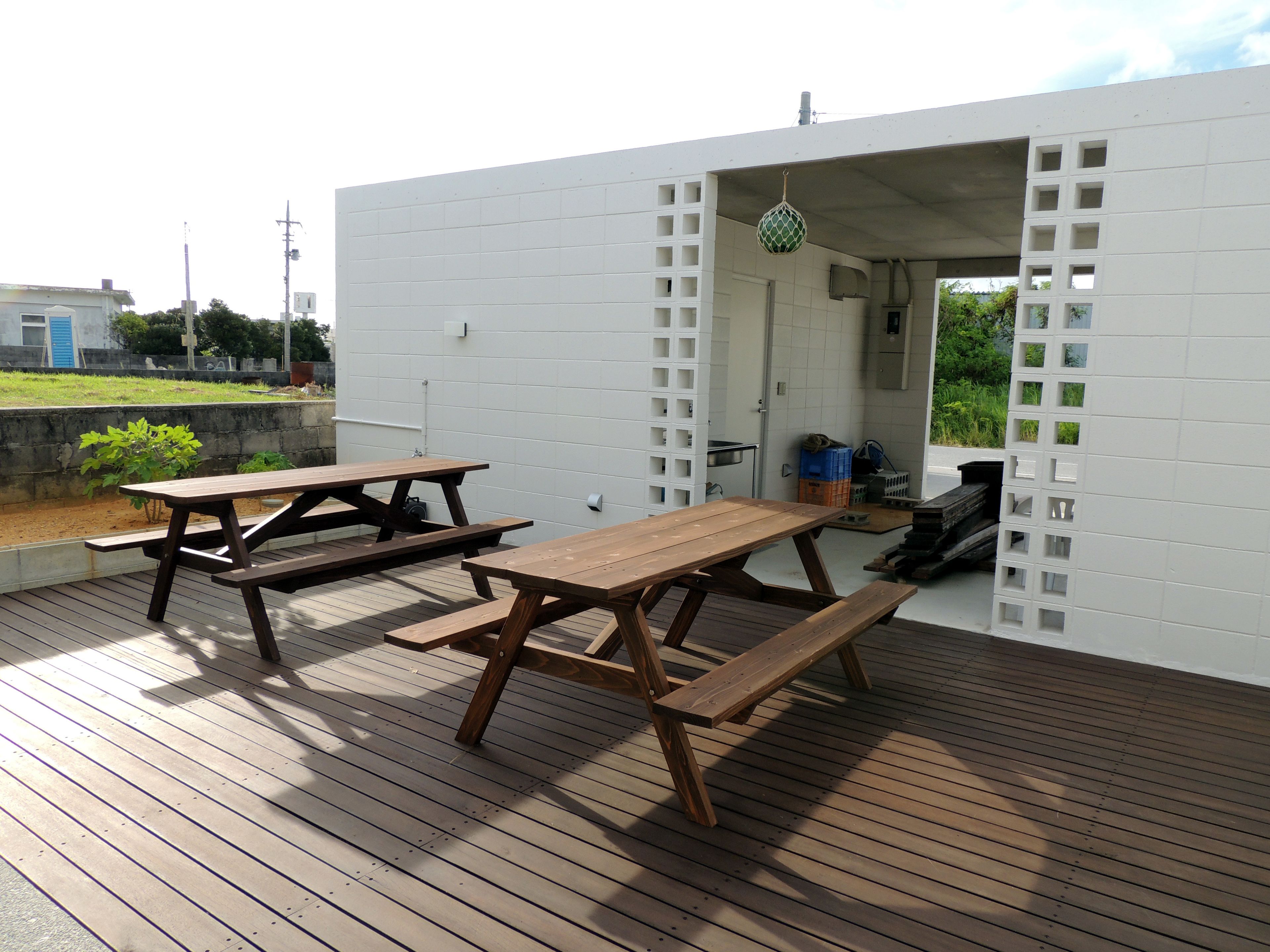 An outdoor wooden deck with picnic tables and a white building with a lattice design.