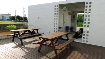 Une terrasse extérieure en bois, dotée de tables de pique-nique, et un bâtiment blanc orné d’un motif en treillis.