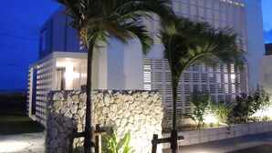 A modern building with a stone wall entrance, palm trees, and a well-lit facade.