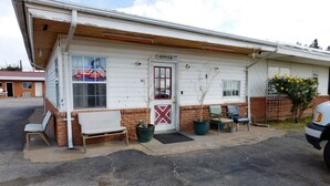 A small building with a sign reading "OFFICE" and a door marked with a red cross. There are two chairs outside, a potted plant, and a small tree. - American Star Inn (Munday)
