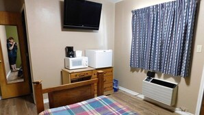 A bedroom with a bed, a dresser, a microwave, a refrigerator, a television, and a window with curtains.
