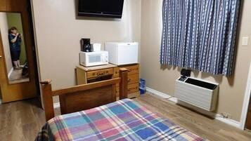 A bedroom with a bed, a dresser, a microwave, a refrigerator, a television, and a window with curtains.