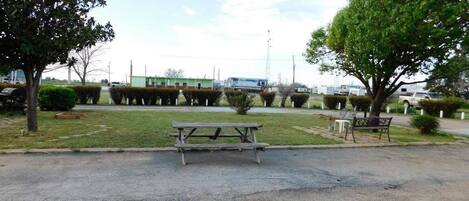 A parking lot with a picnic table and benches, surrounded by trees and a building in the background.