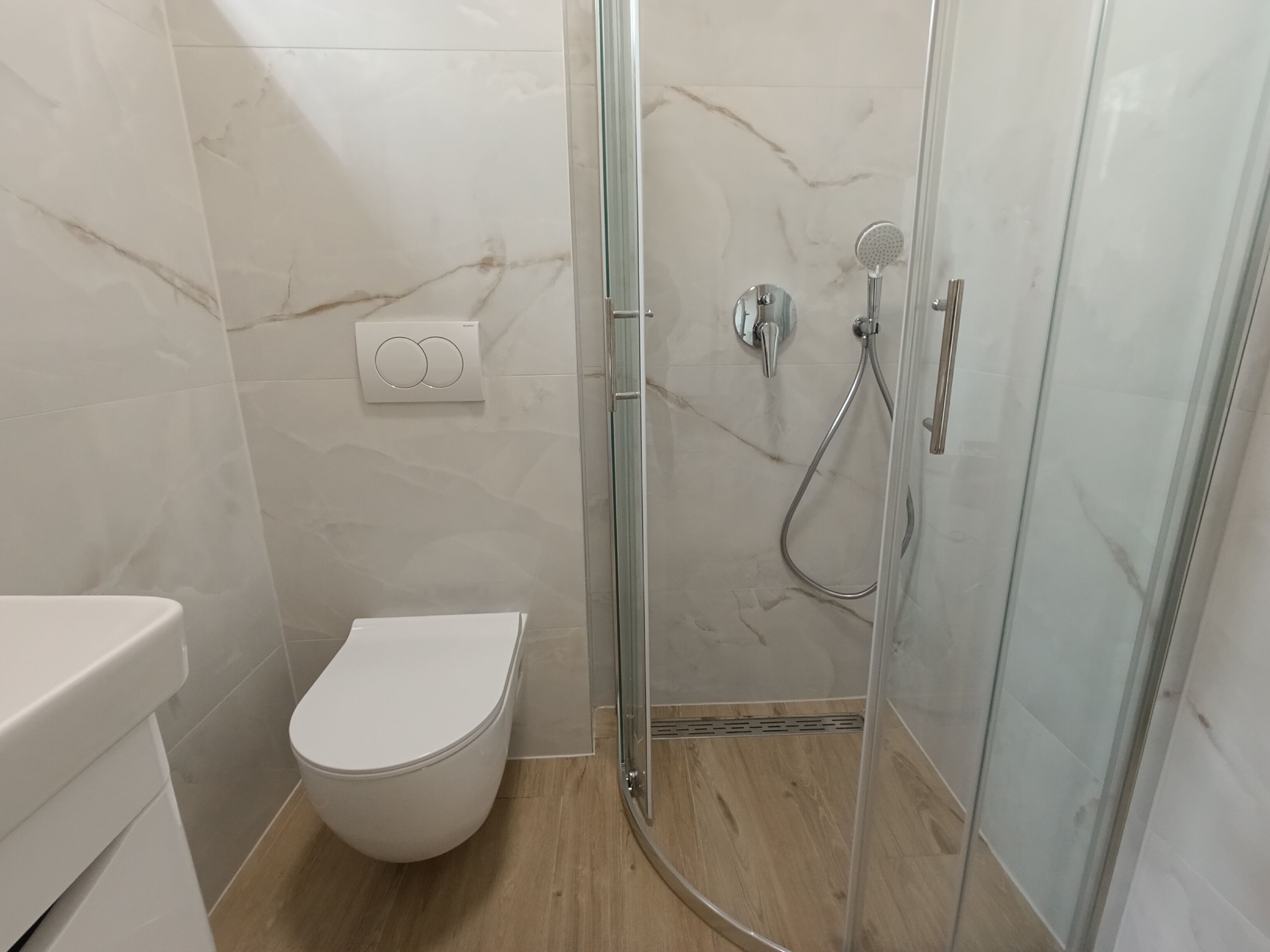 Ein Badezimmer mit Toilette, einer Duschkabine mit Glastür und einer an der Wand montierten Bedienkonsole.