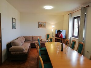 A cozy living room with a sofa, a dining table with chairs, a TV, and a lamp.