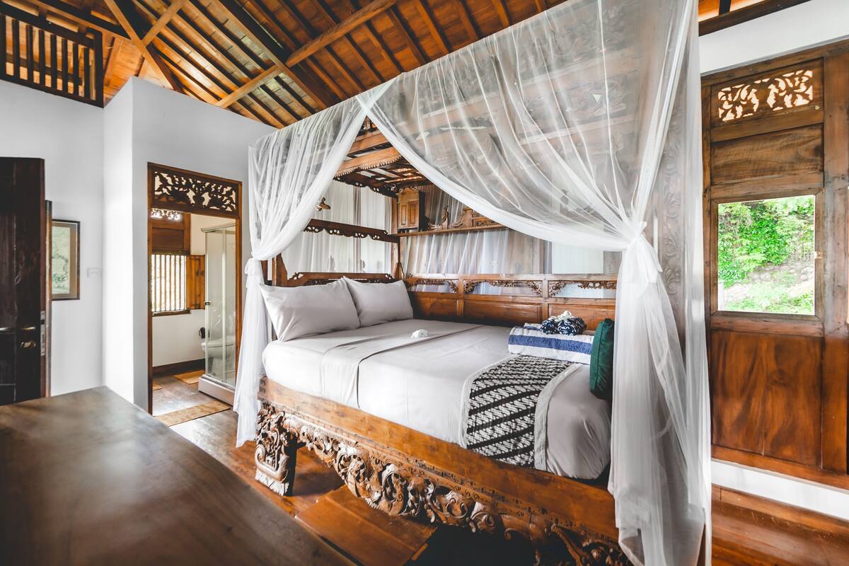 A bedroom with a wooden bed frame, white bedding, and a canopy.