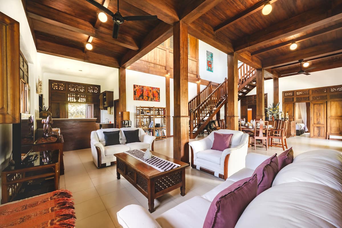 A spacious living area with a high ceiling, wooden beams, and a staircase leading to an upper level.