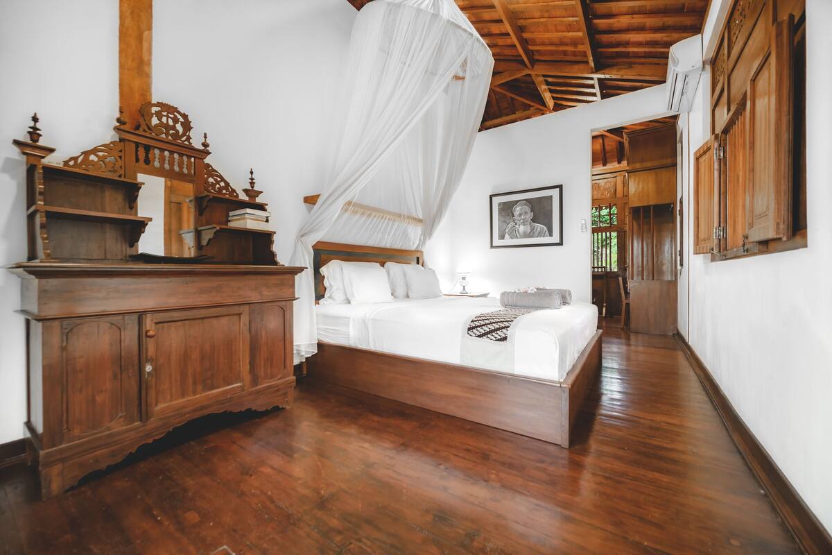 A bedroom with a wooden bed, a nightstand, a wardrobe, and a canopy bed.