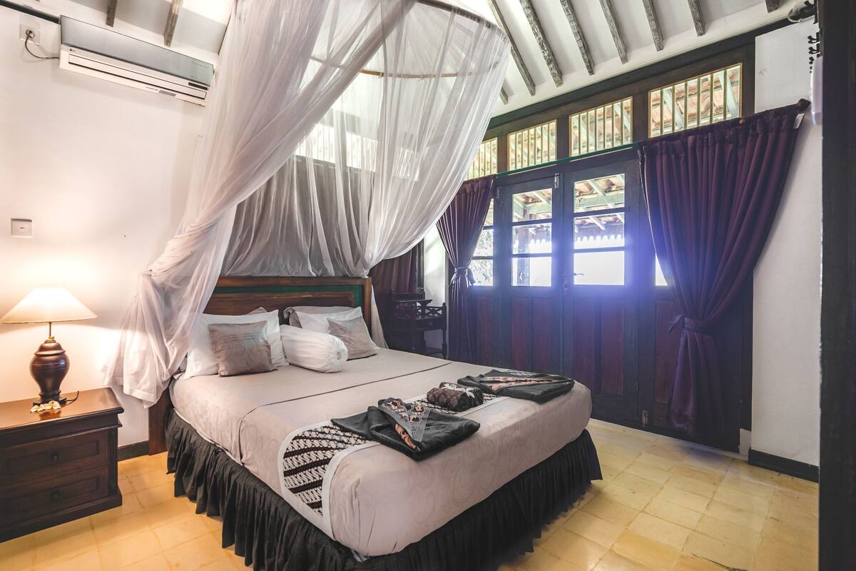 A bedroom with a bed, bedside table, lamp, and curtains.