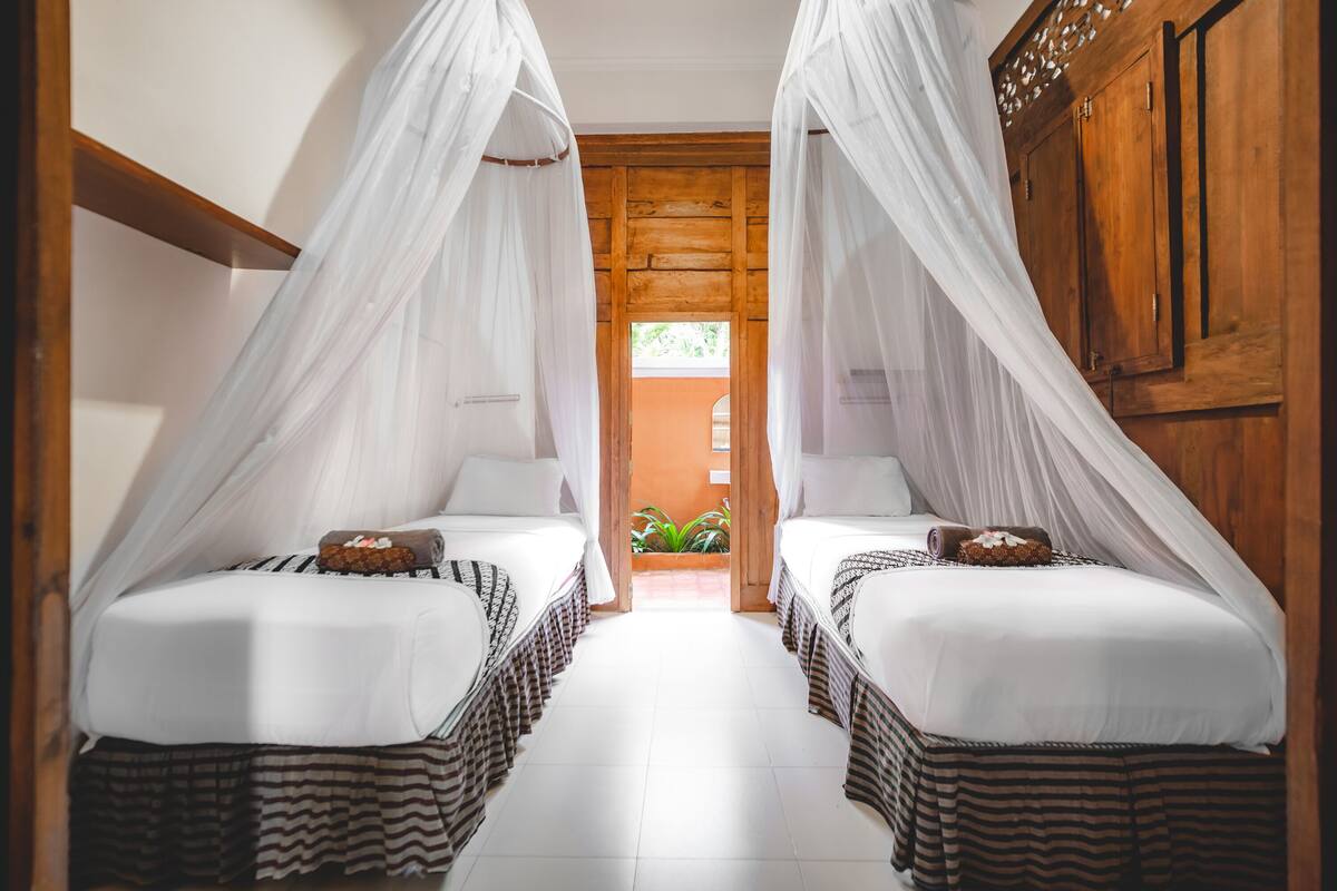 A room with two beds, each with a canopy, and a wooden door leading to a balcony.