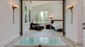 A modern bathroom with a large bathtub, a shower area, and a window providing natural light. - Waterfall Manor | Mountain Luxury w/ Fireplaces & Views + Biltmore Pass (Fletcher)