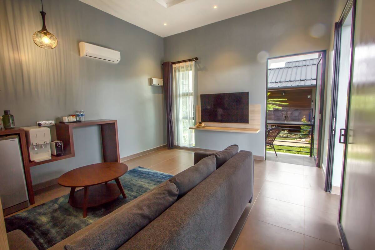 A modern living room with a sofa, a coffee table, and a TV mounted on the wall. There is a sliding glass door leading to an outdoor area.