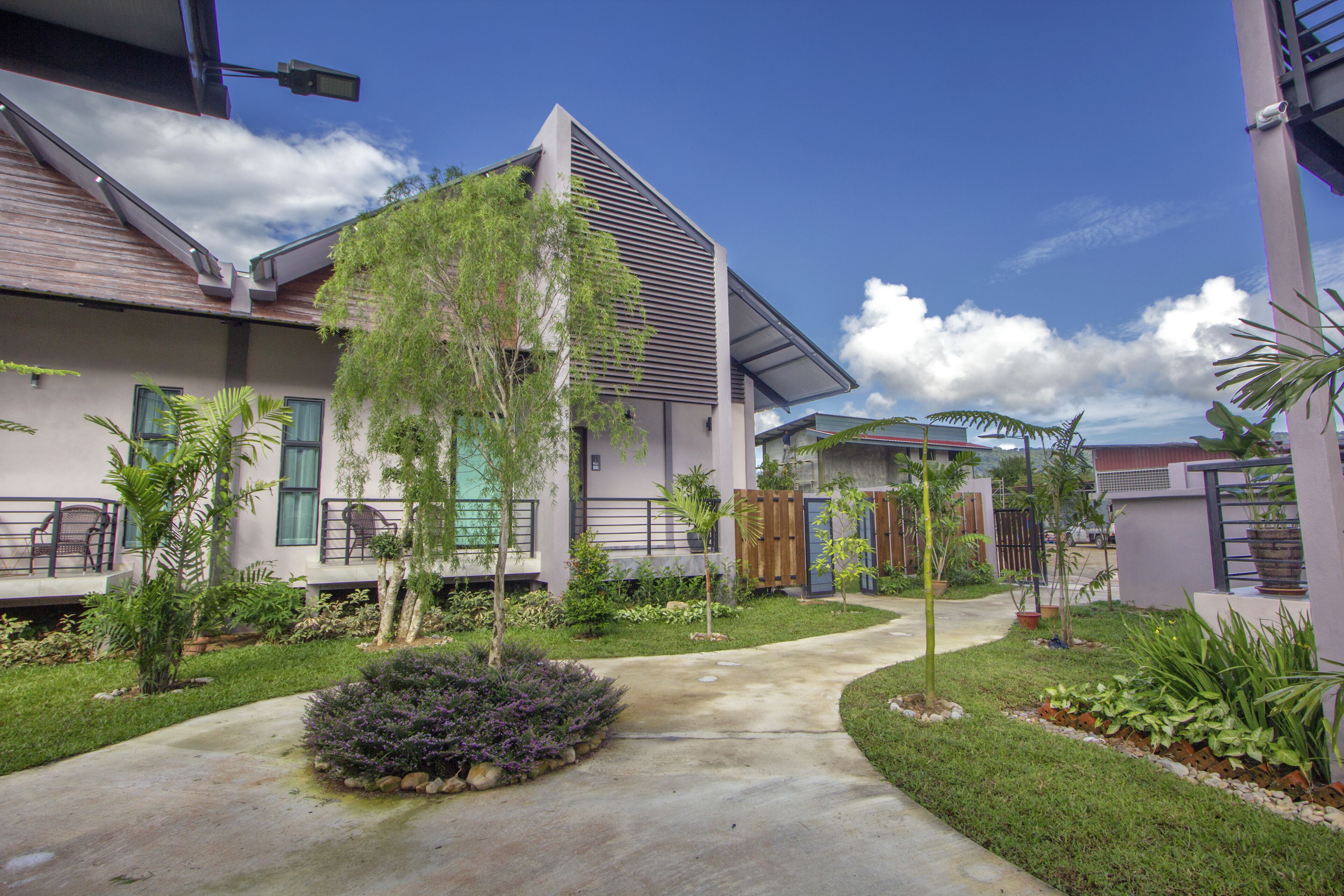 A modern residential building with a sloped roof, a covered patio, and a well-maintained garden with various plants and a pathway.