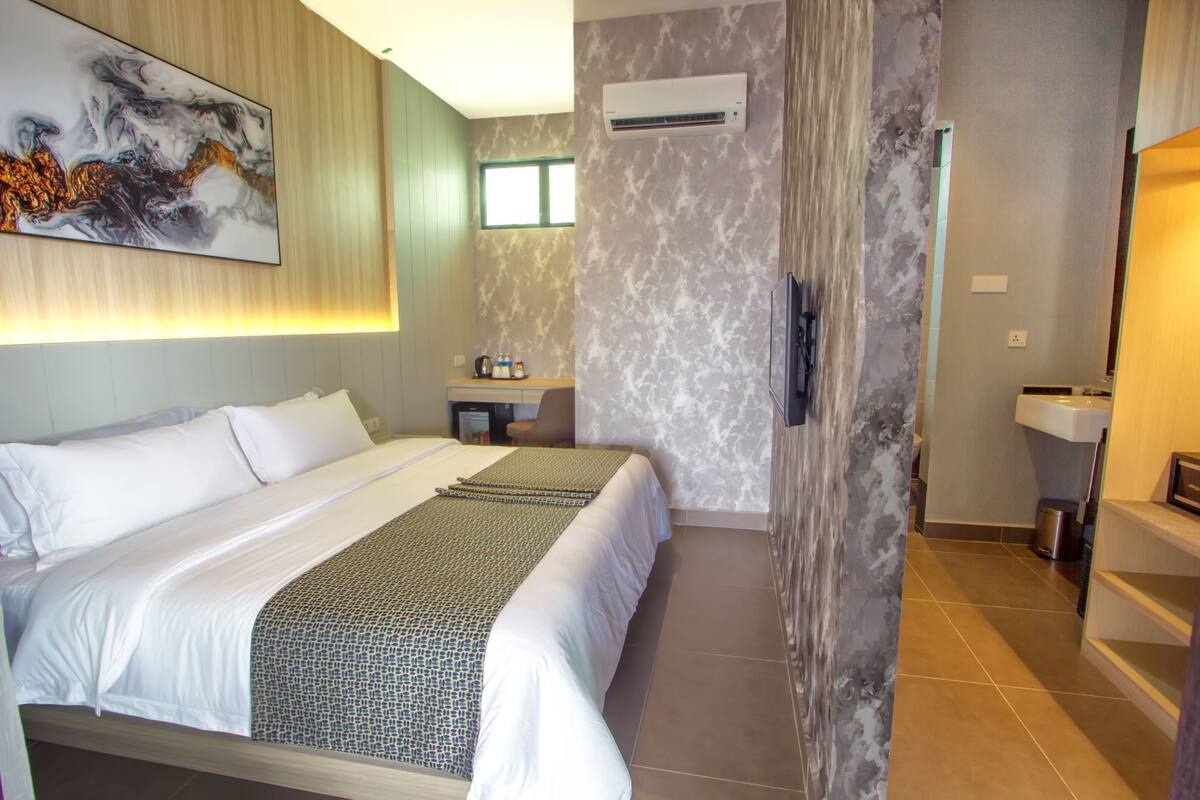A modern hotel room with a large bed, a bathroom with a sink and mirror, and a wall-mounted air conditioner.