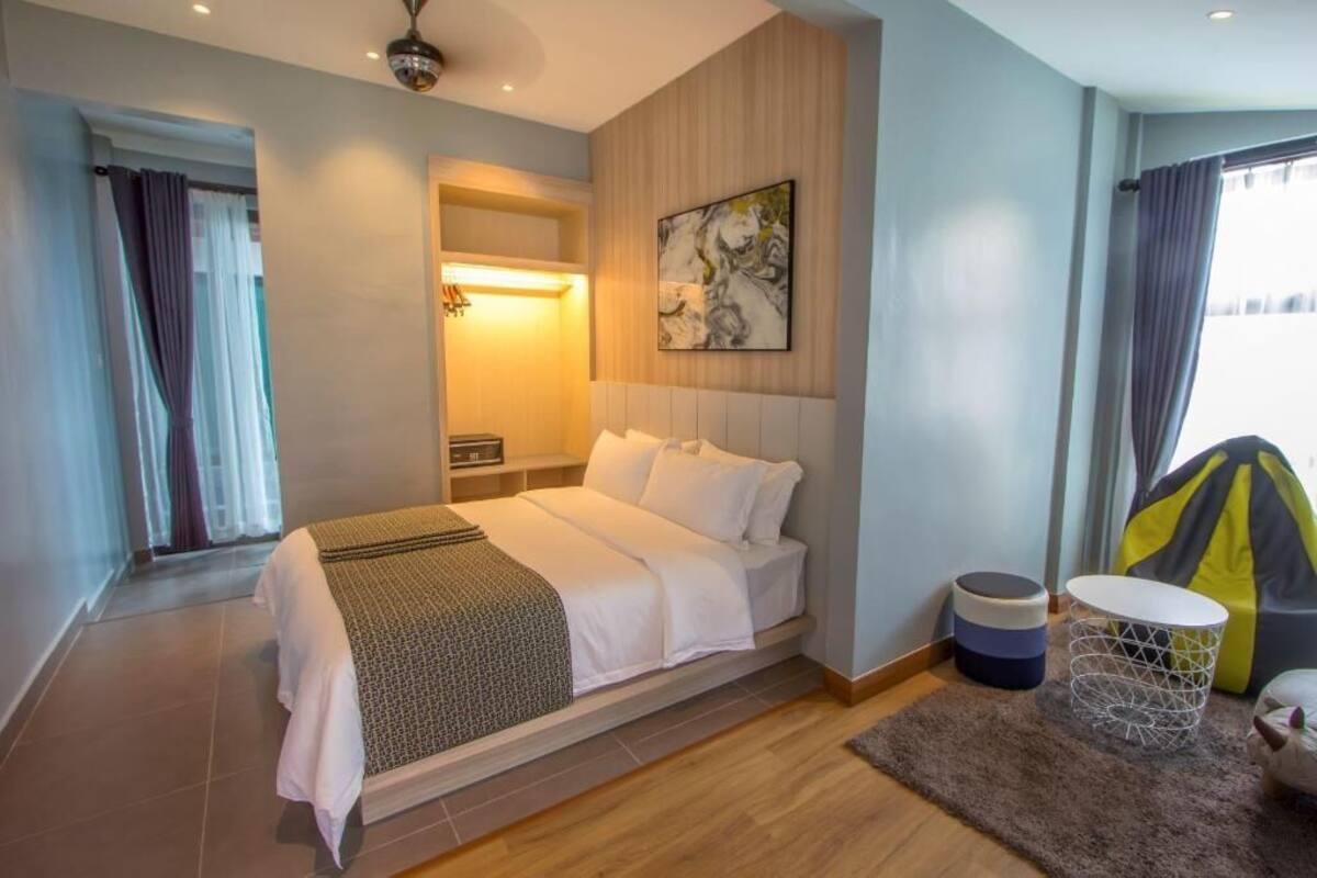 A hotel room with a bed, bedside table, lamp, artwork, and a view of the outdoors.