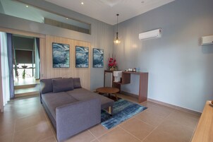 Una sala de estar moderna con un sofá gris, una mesita redonda pequeña y un tapete azul. Hay tres cuadros abstractos en la pared, una lámpara colgante y un equipo de aire acondicionado.