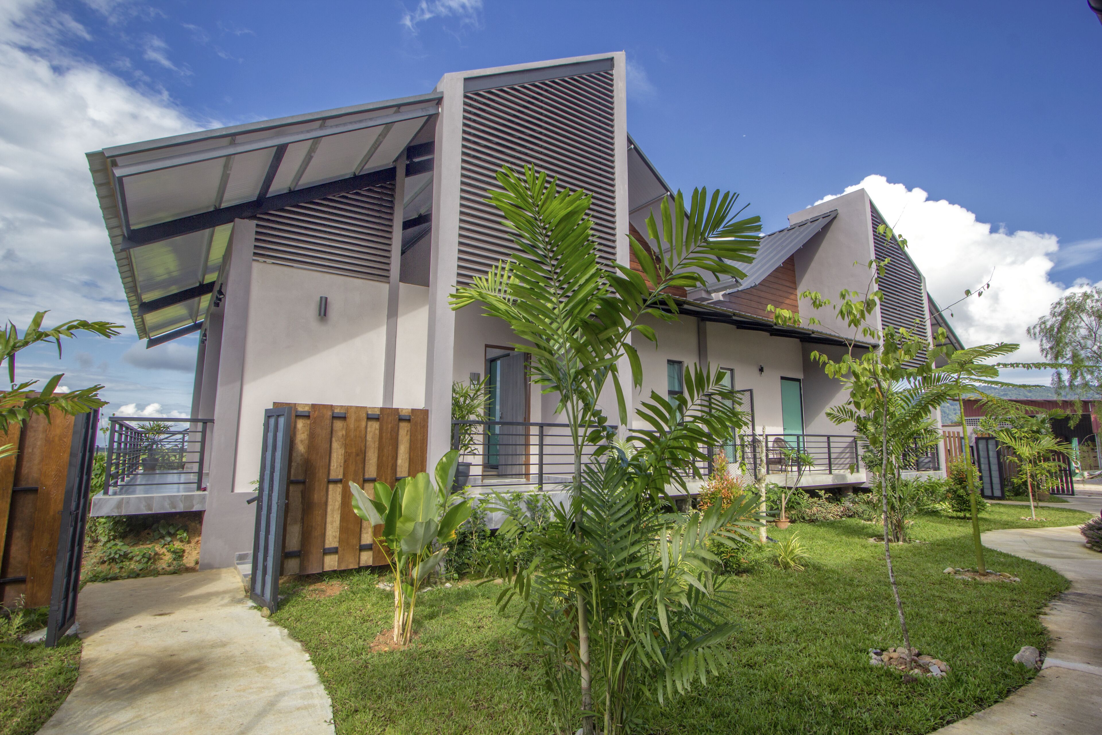 A modern two-story house with a flat roof, a covered porch, and a well-maintained garden with various plants and a pathway leading to the entrance.