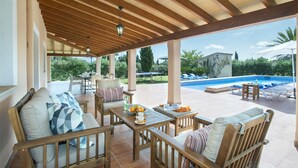 A covered outdoor seating area with wooden furniture, a pool, and a view of the surrounding greenery. - VILLA ROMEU - 10 MIN WALK TO THE OLD TOWN (Pollensa)
