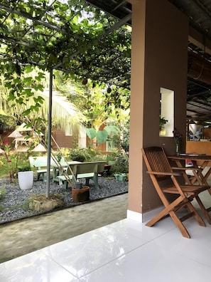 A covered outdoor seating area with a table and chairs, surrounded by plants and a gravel path. - Phuc Sinh Homestay (Phu Tuc)