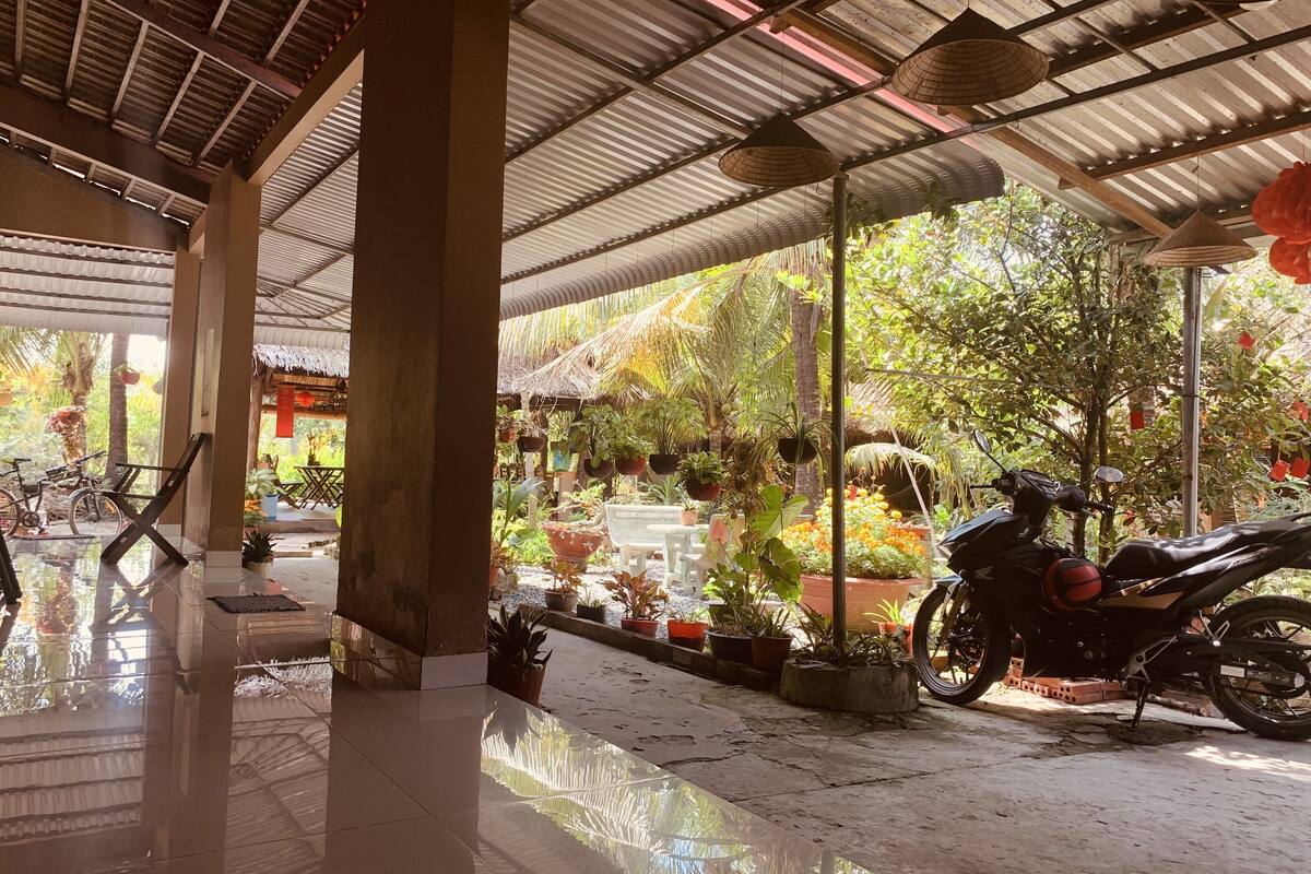 Un espacio al aire libre techado, con suelo de baldosas, plantas en macetas y una motocicleta estacionada.