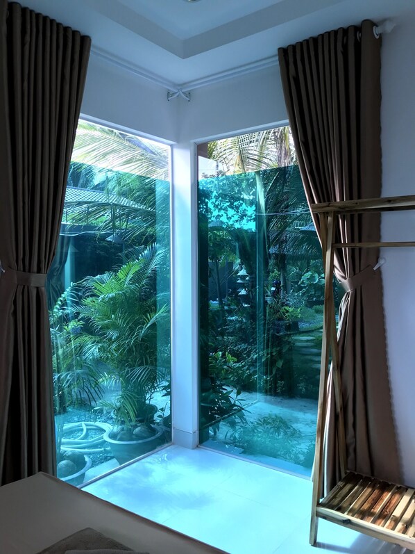 A room with a large glass door leading to a garden. - Phuc Sinh Homestay (Chau Thanh)