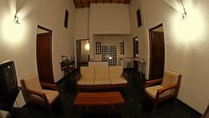 A room with a sofa, two armchairs, a wooden bench, a television, and a wall-mounted light fixture. - Primrose Bungalow (Kandy)