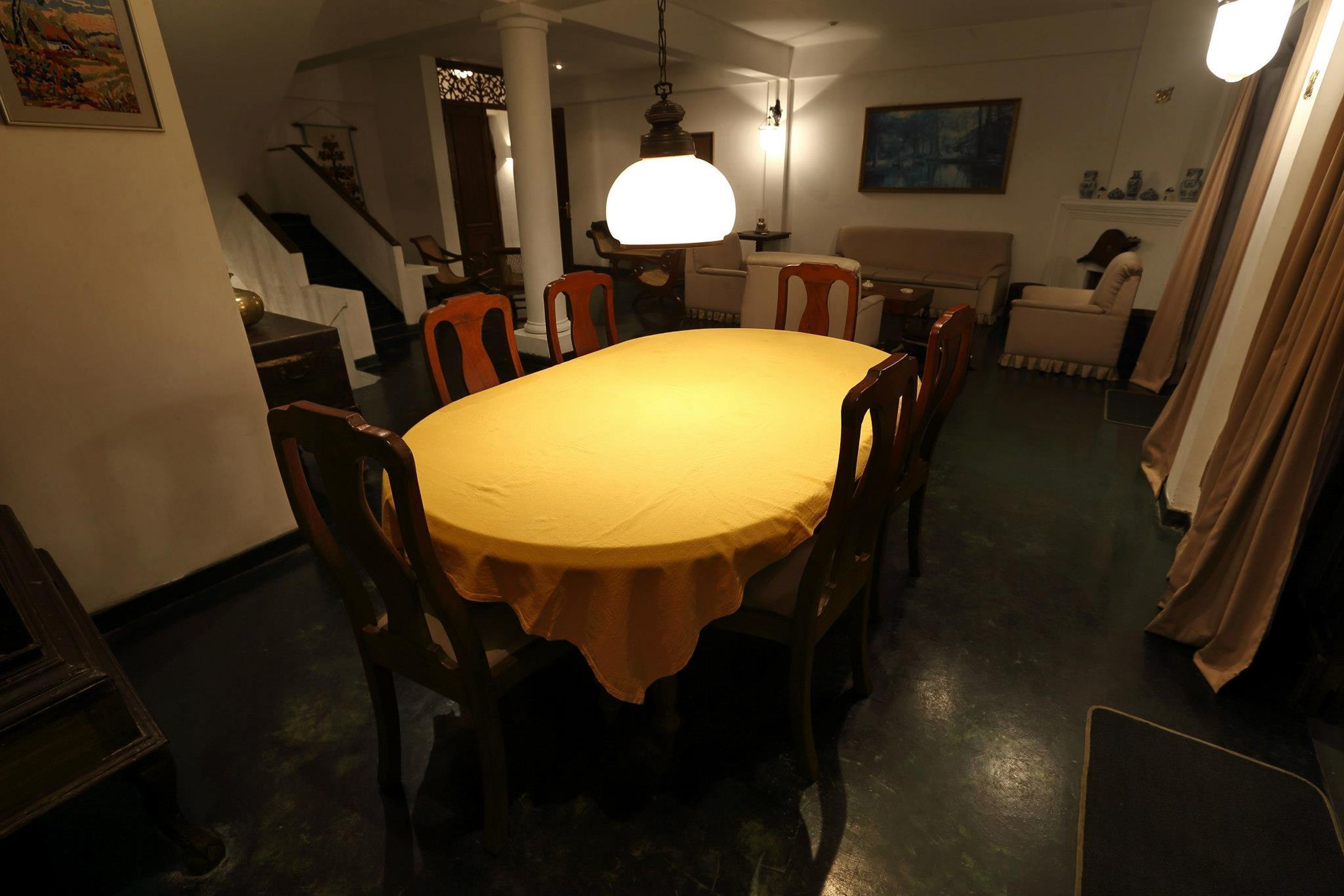 A dining area with a round table covered in a yellow tablecloth, surrounded by wooden chairs.