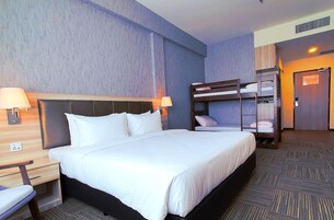 Habitación de hotel con una cama grande, dos mesitas de noche con lámparas, una litera y un armario.