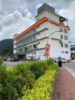 Un hotel de varios pisos con un letrero llamativo que dice "Maple Lodge", un estacionamiento con varios coches y una zona ajardinada al frente.