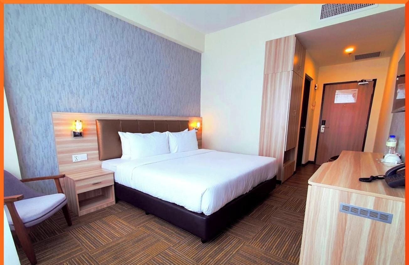 Habitación de hotel con cama, mesita de noche, silla y escritorio con teléfono.